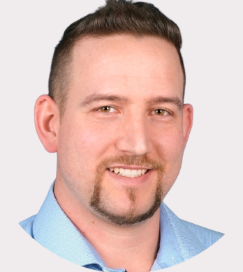 Ein Mann mit kurzen Haaren und einem breiten Lächeln, trägt ein hellblaues Hemd.