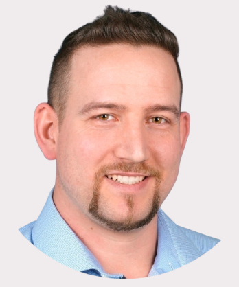 Mann mit kurzem, blondem Haar und Bart, lächelt vor blauem Hintergrund.