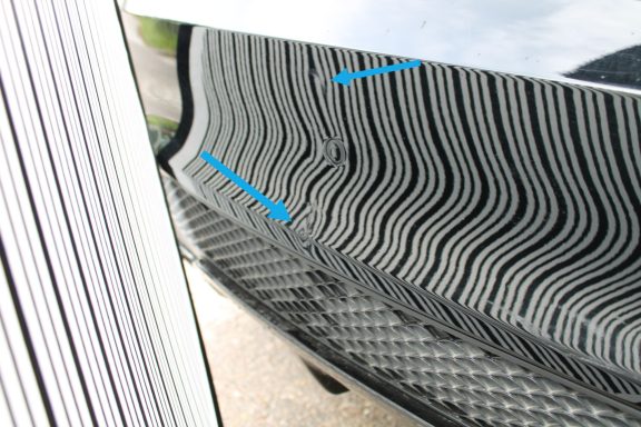 Dellensegel zeigt Verformung des Materials Nahaufnahme einer spiegelnden Oberfläche mit gewellten Mustern und zwei blauen Pfeilen.