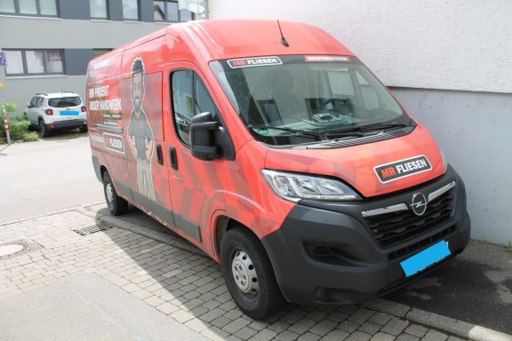 Ansicht vorne rechts Roter Lieferwagen mit Werbung, geparkt an einer lichten Straße.