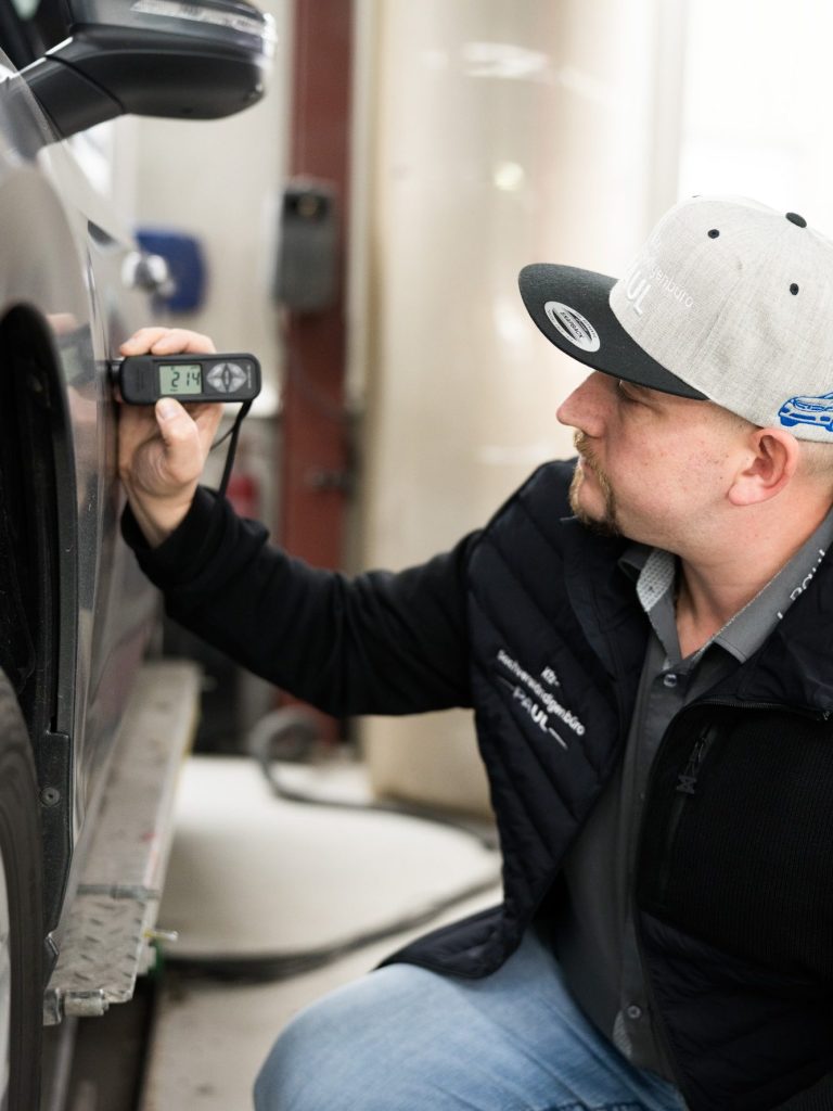 Ein Mann misst die Dicke des Lacks an einem Auto mit einem Messgerät.