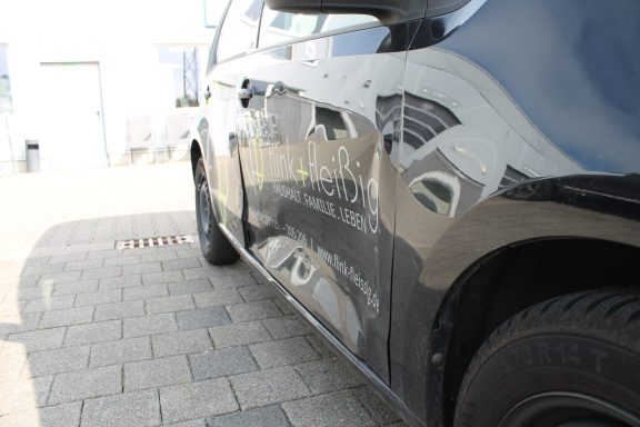 Seitenschaden Übersicht Schwarzes Auto mit Delle an der linken Seite, reflektiert umgebende Gebäude.