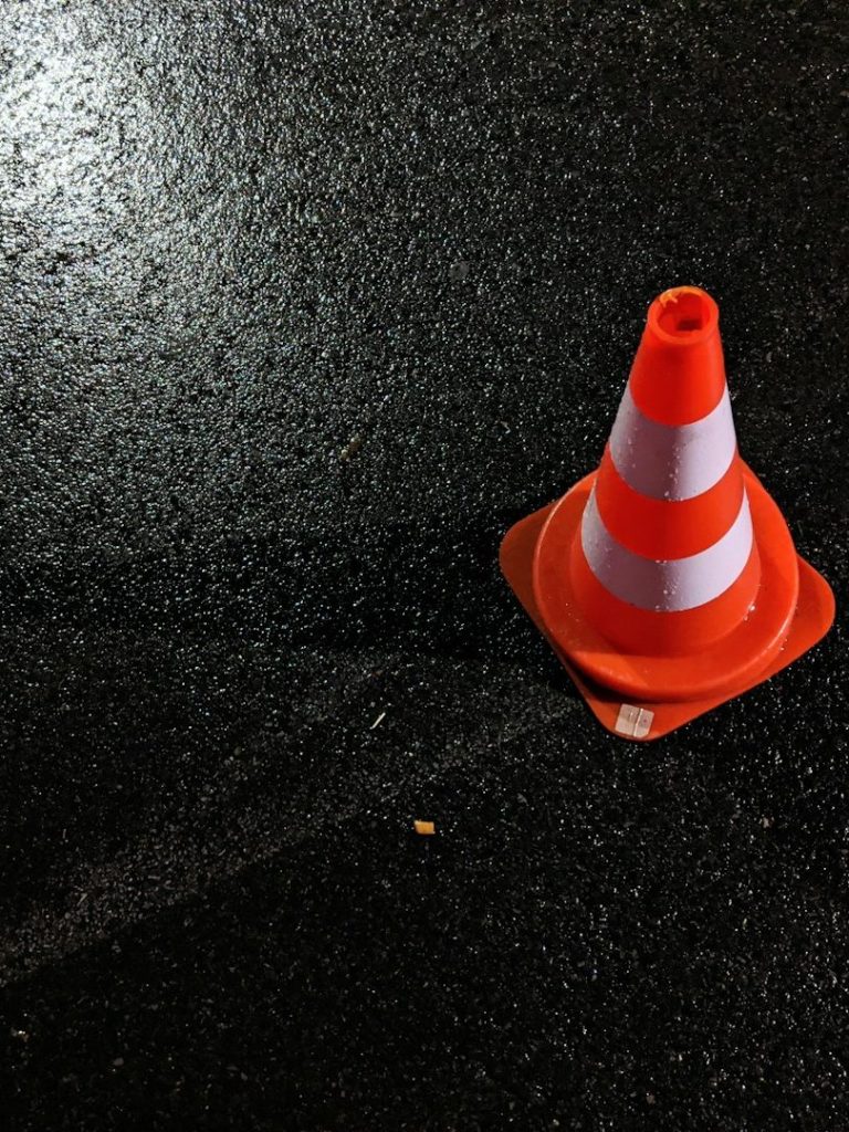 Oranger Verkehrscone mit weißen Streifen auf nasser Straße.