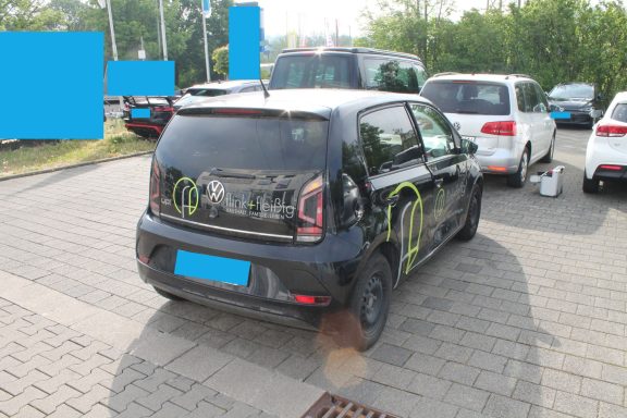 VW UP Seitenschaden rechts Schwarzes Auto mit grüner Markierung auf der Heckklappe, parkt auf einem Parkplatz.